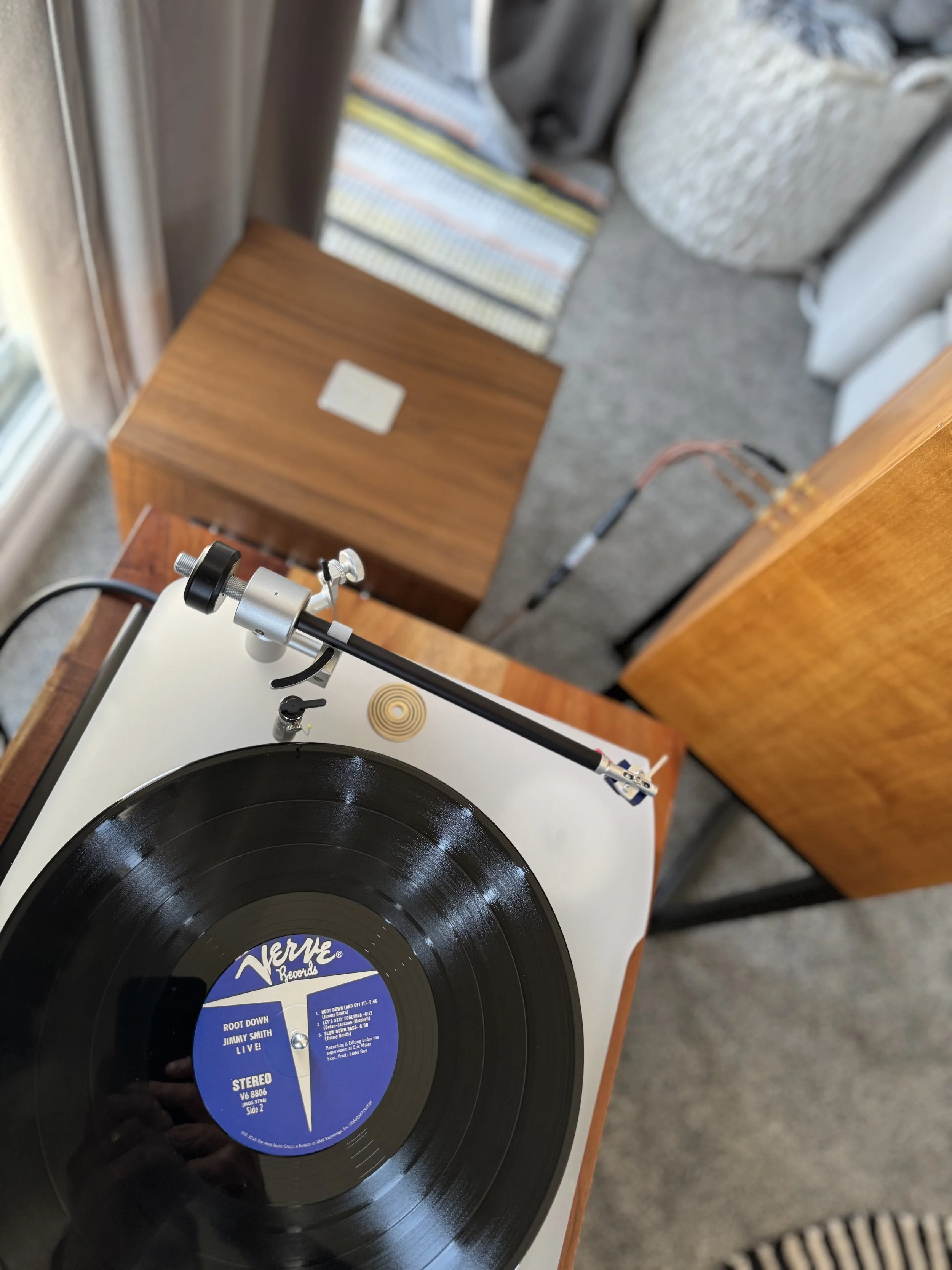 Close-up of a vintage turntable playing a vinyl record titled 'Root Down' by Jimmy Smith, with a wooden side table and patterned carpet visible in the background.