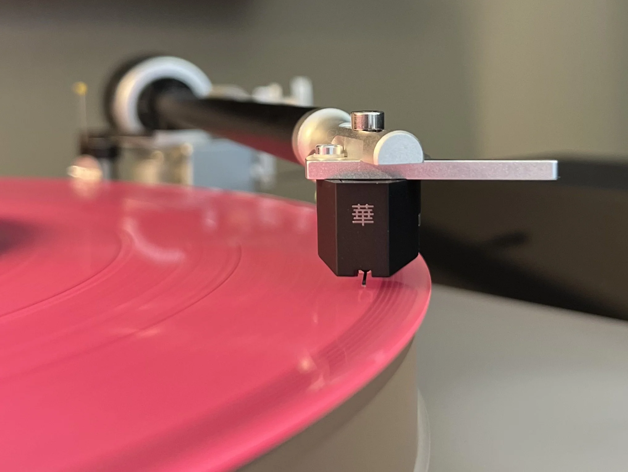 Close-up of a turntable's tonearm and cartridge playing a pink vinyl record.