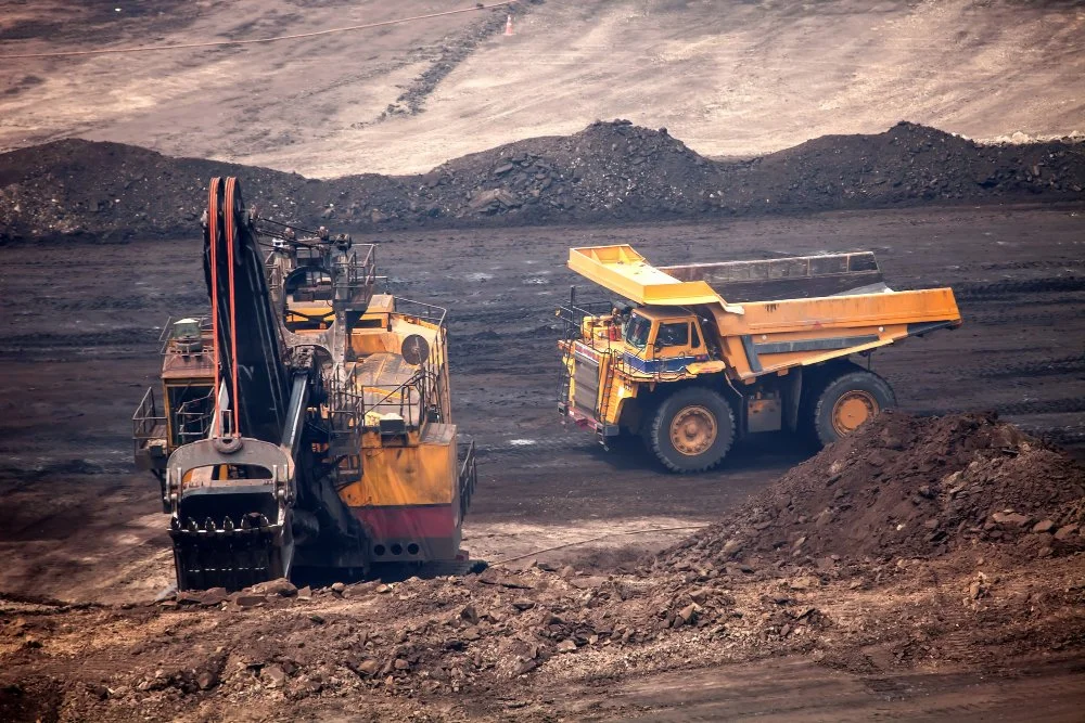 Photo of two large mining trucks working on a barren, dusty landscape with piles of earth and rocks.