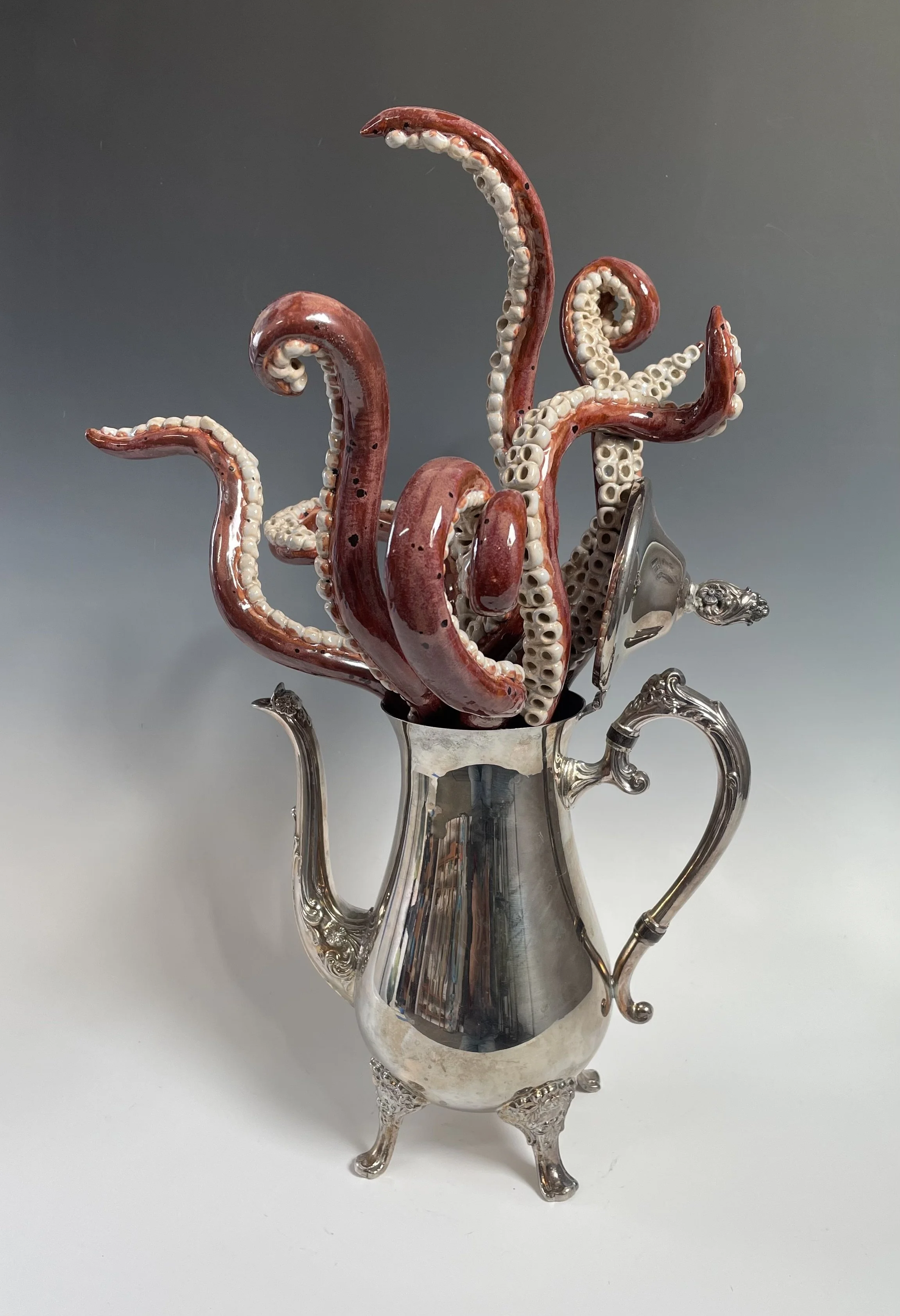 This is an antique silver coffee pot with a ceramic octopus emerging from the top. The legs are waving around as it figures out about coming out.