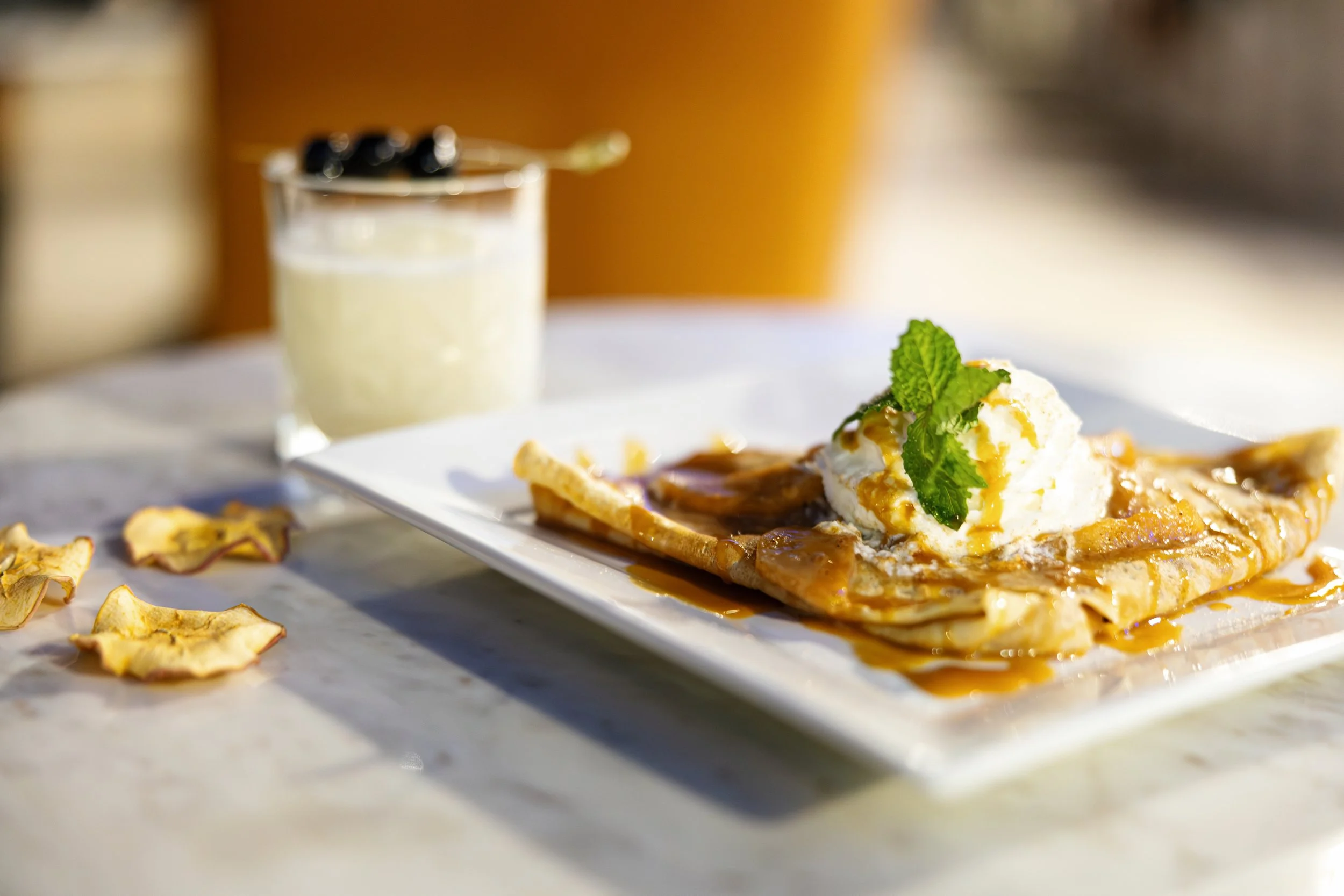 A dessert crepe topped with a scoop of vanilla ice cream and fresh mint, drizzled with caramel sauce, served on a white plate.