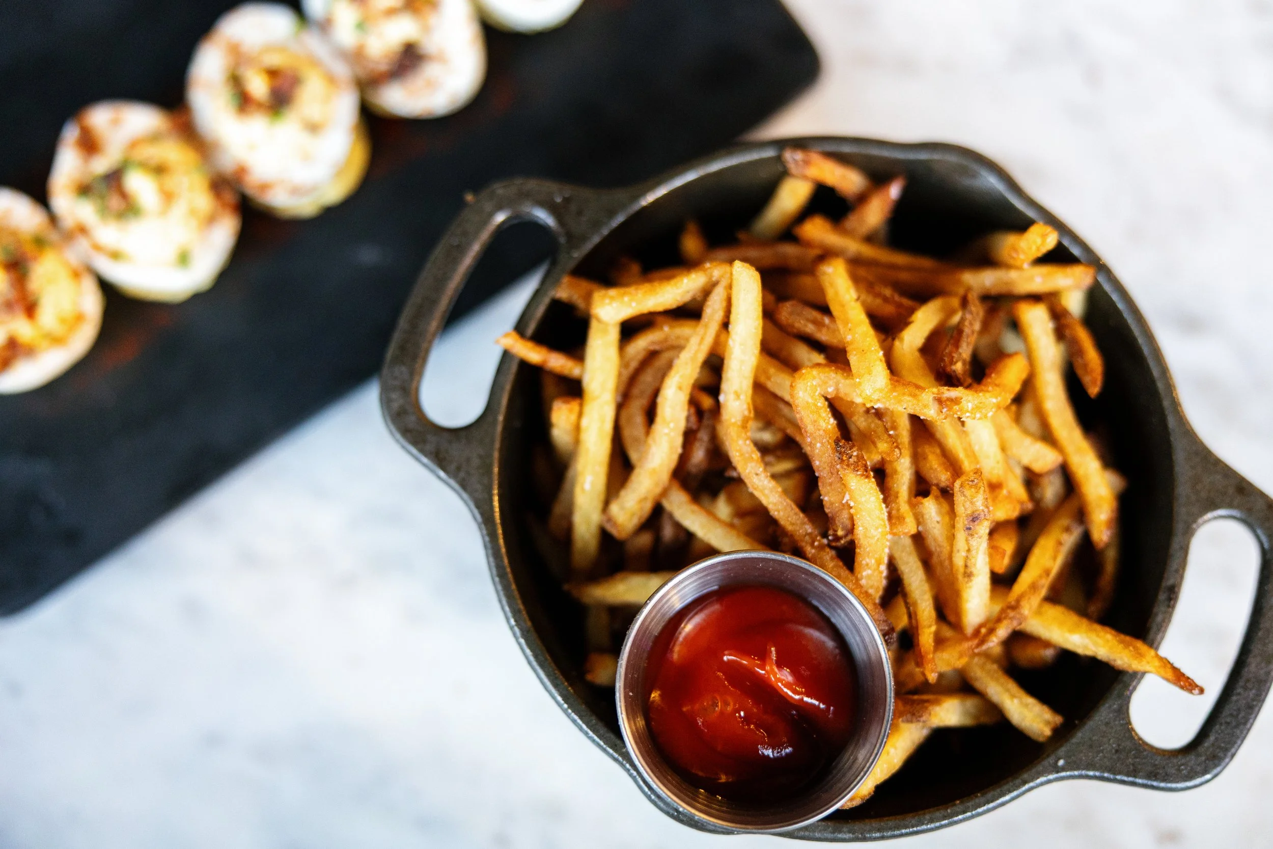 Basket of French fries with ketchup and a plate of sushi rolls in the background.