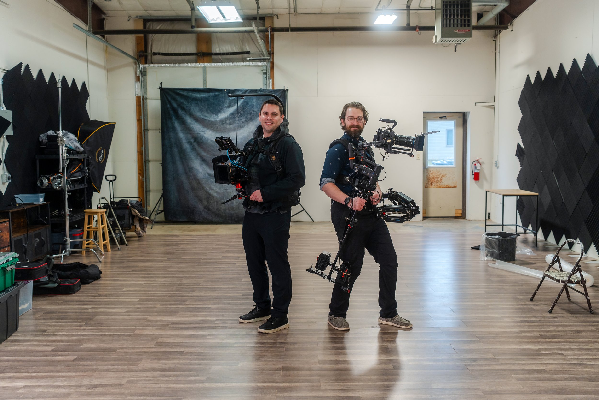 Ben Tierney-Morrison of Morrison Media, LLC holding a sony video camera on an easy rig with a monitor and tripod legs. Jacob Zabinski stands next to him with his laowa lens and lumix camera on his easyrig.