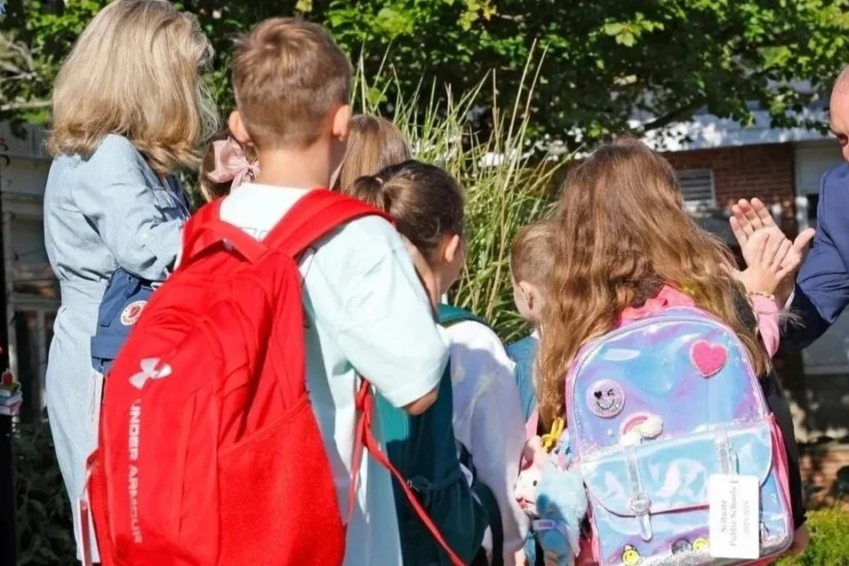 Group of children with backpacks standing outdoors, engaged in conversation, possibly during a school trip or outdoor activity.