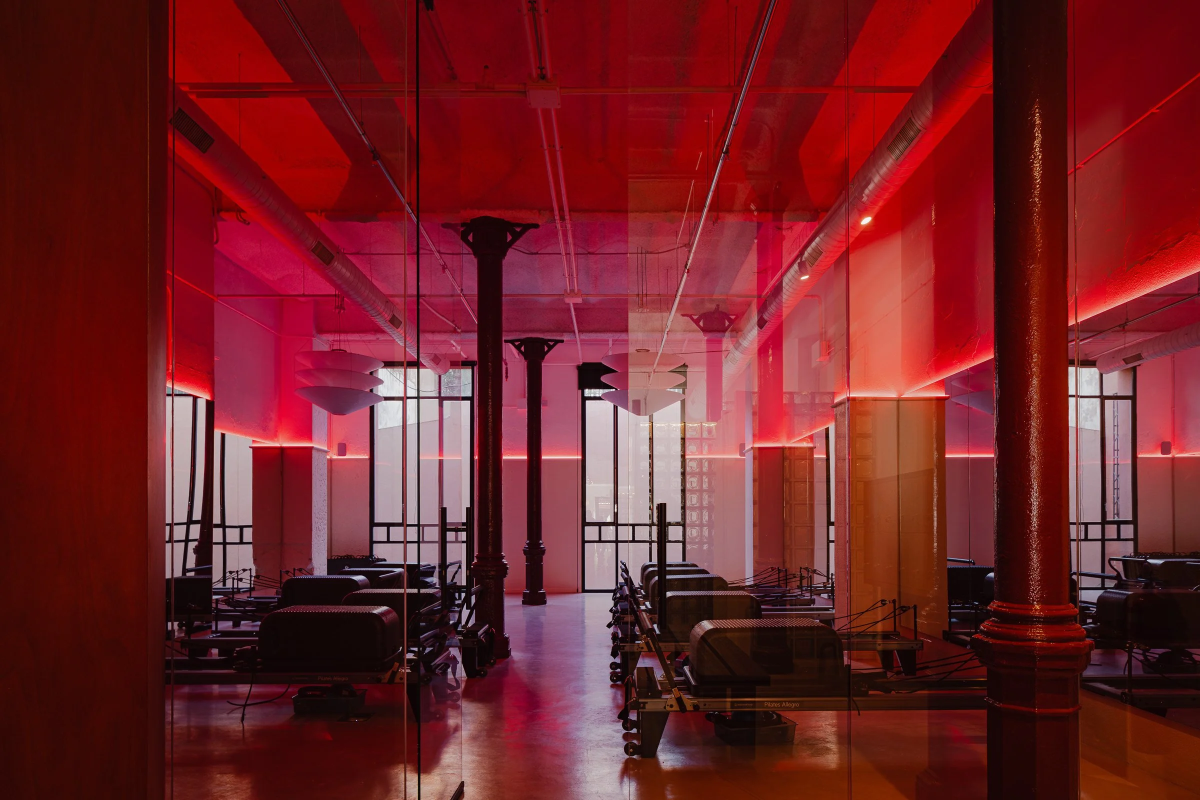 Beautiful reformer pilates studio with high ceilings, steel columns and a red glow.