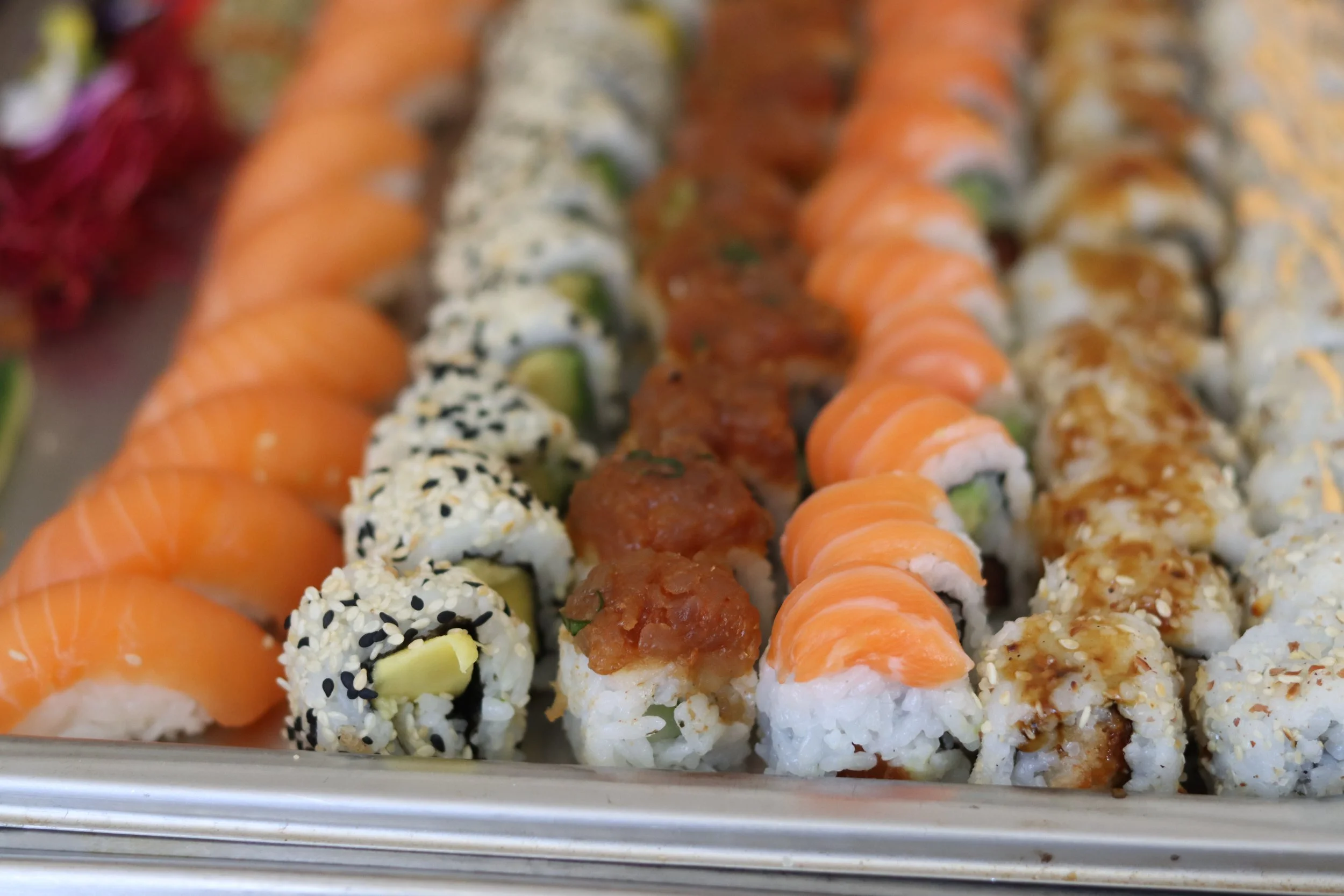 Verschiedene Sushi-Rollen in einem Sushi-Tablett, darunter Rollen mit Lachs, Sesam, Avocado und frische Zutaten.