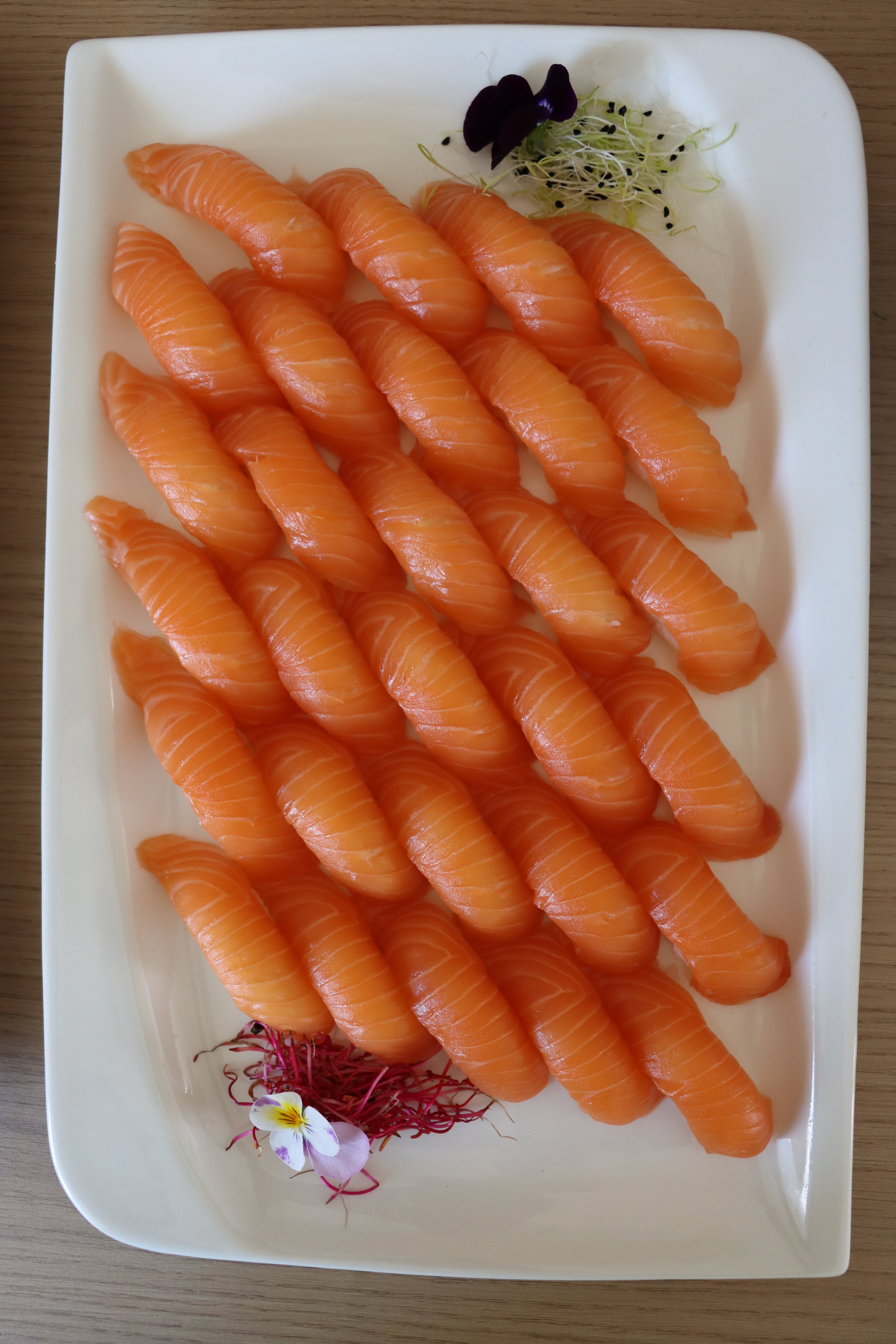 Sashimi-Lachs auf einem weißen Teller mit Dekoration aus Sprossen, eine kleine Blume und essbarer Orchidee.
