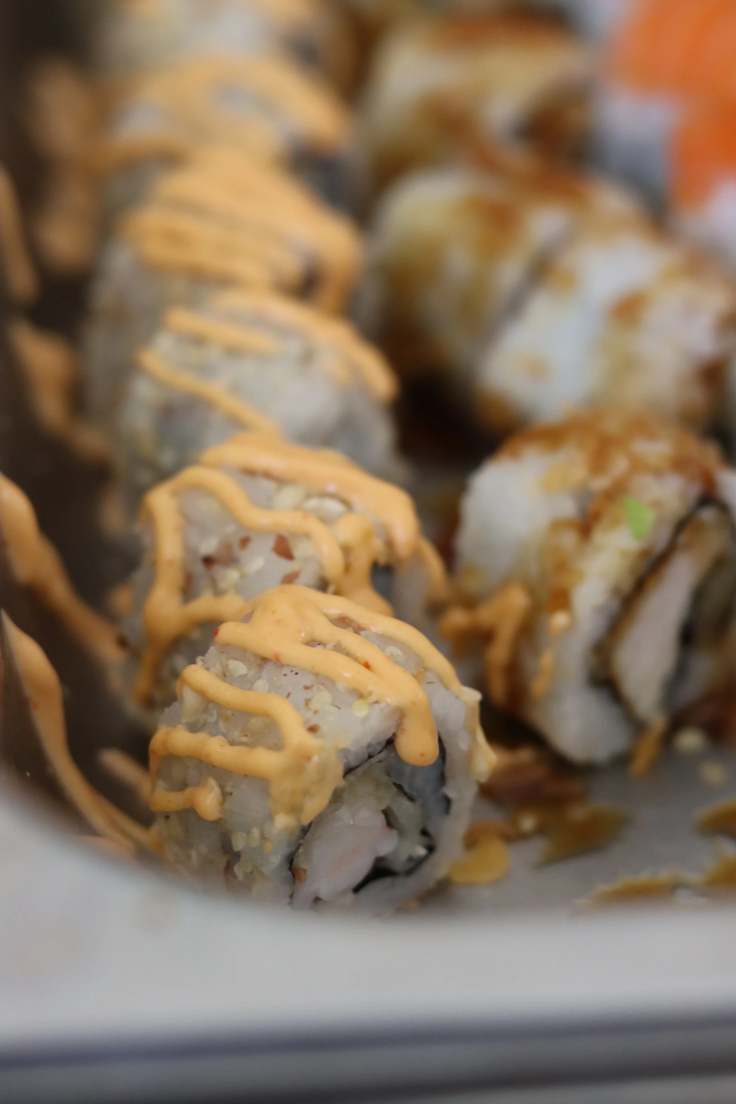 Nahaufnahme von Sushi-Rollen mit weißem Reis, mit Honig-Senf-Drizzle und einem grünen Beilagenblatt.