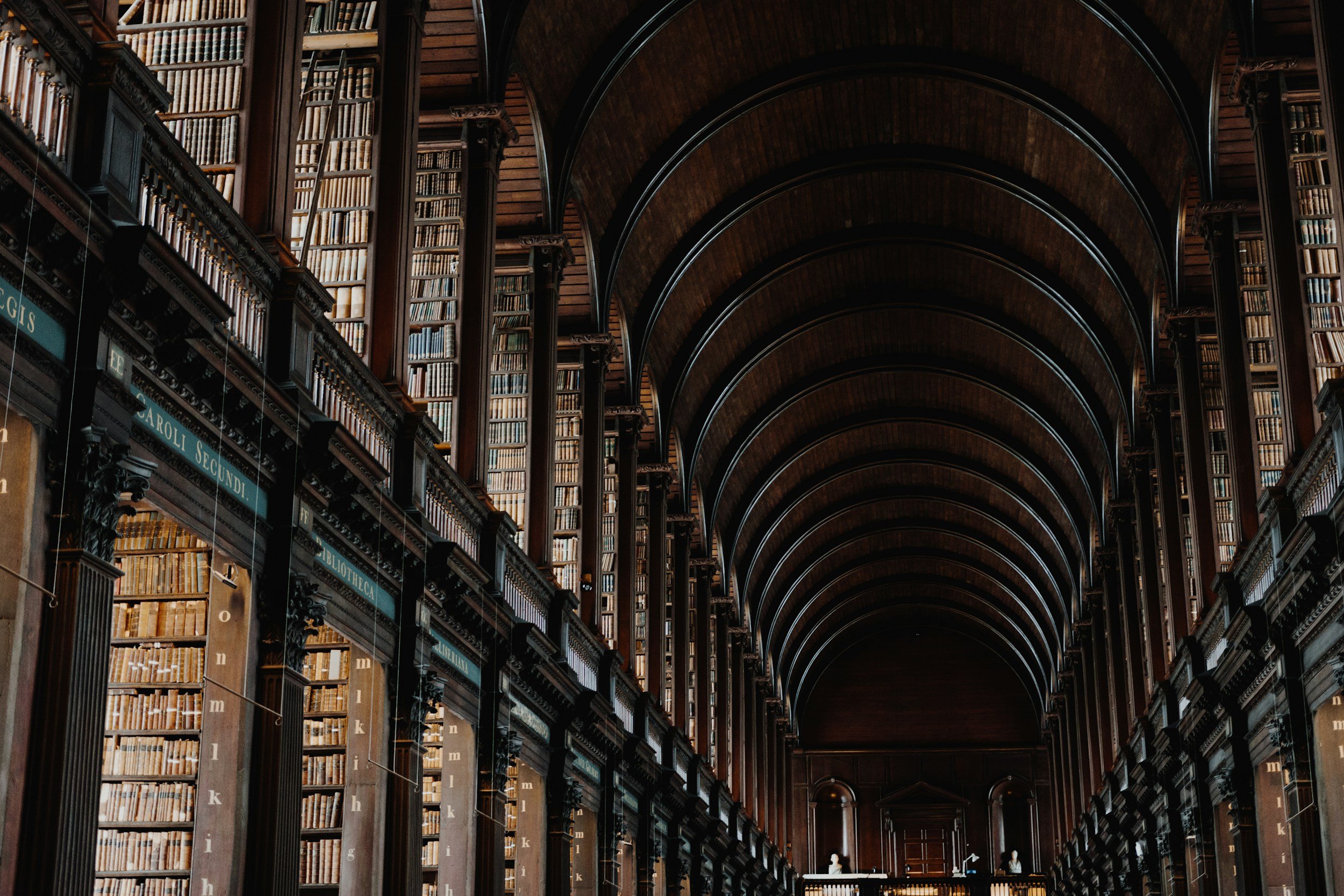 Interior of a grand, historic library with dark wood shelves and arched ceilings, filled with rows of books on multiple levels.