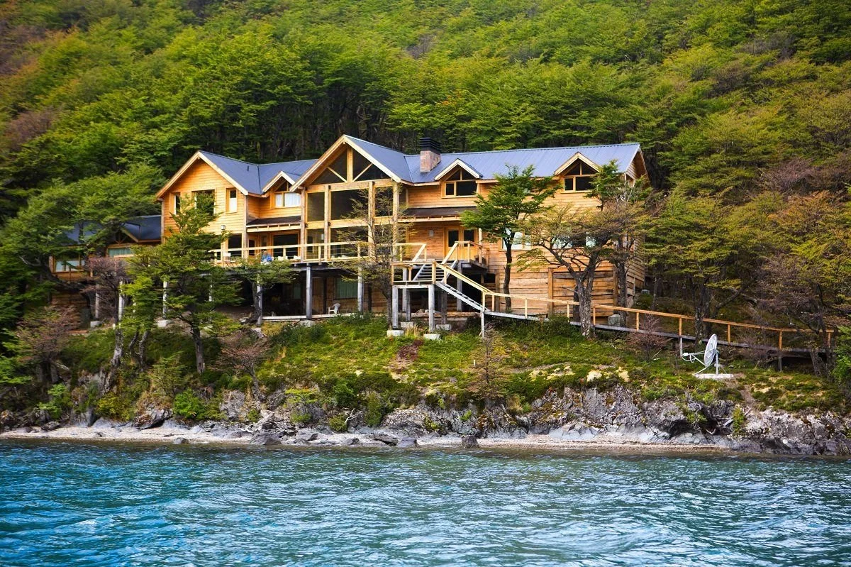 Wooden house on a hillside overlooking a body of water, surrounded by trees.