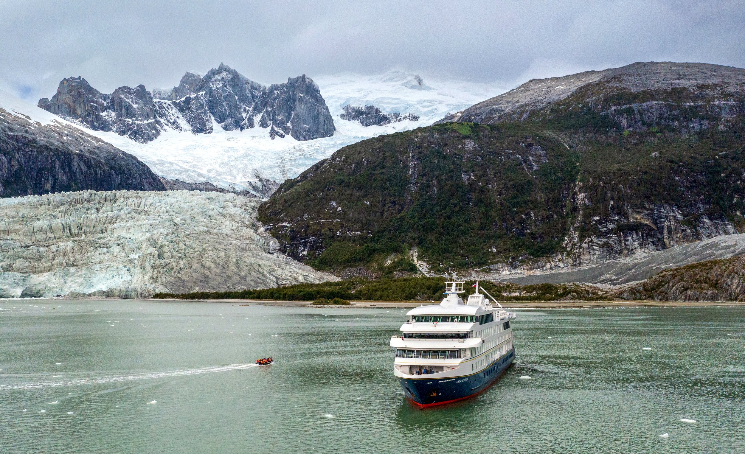 A cruise ship sailing in a glacial landscape with snow-capped mountains and icebergs in the water.
