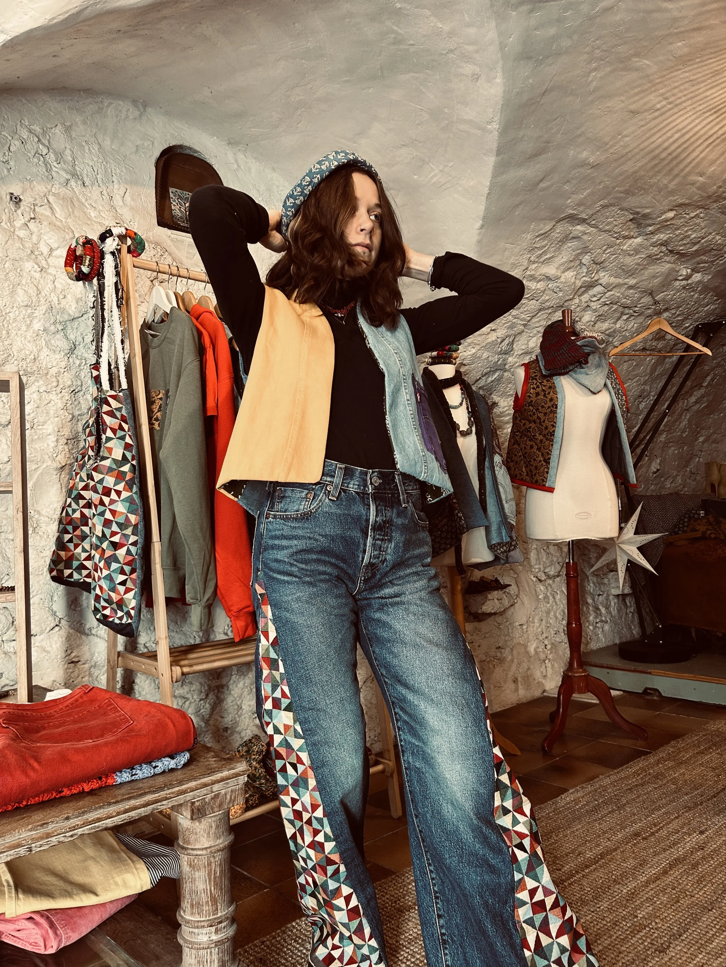 Une femme adjusting un bonnet dans une boutique de vêtements vintage, entourée de vêtements et accessoires colorés.