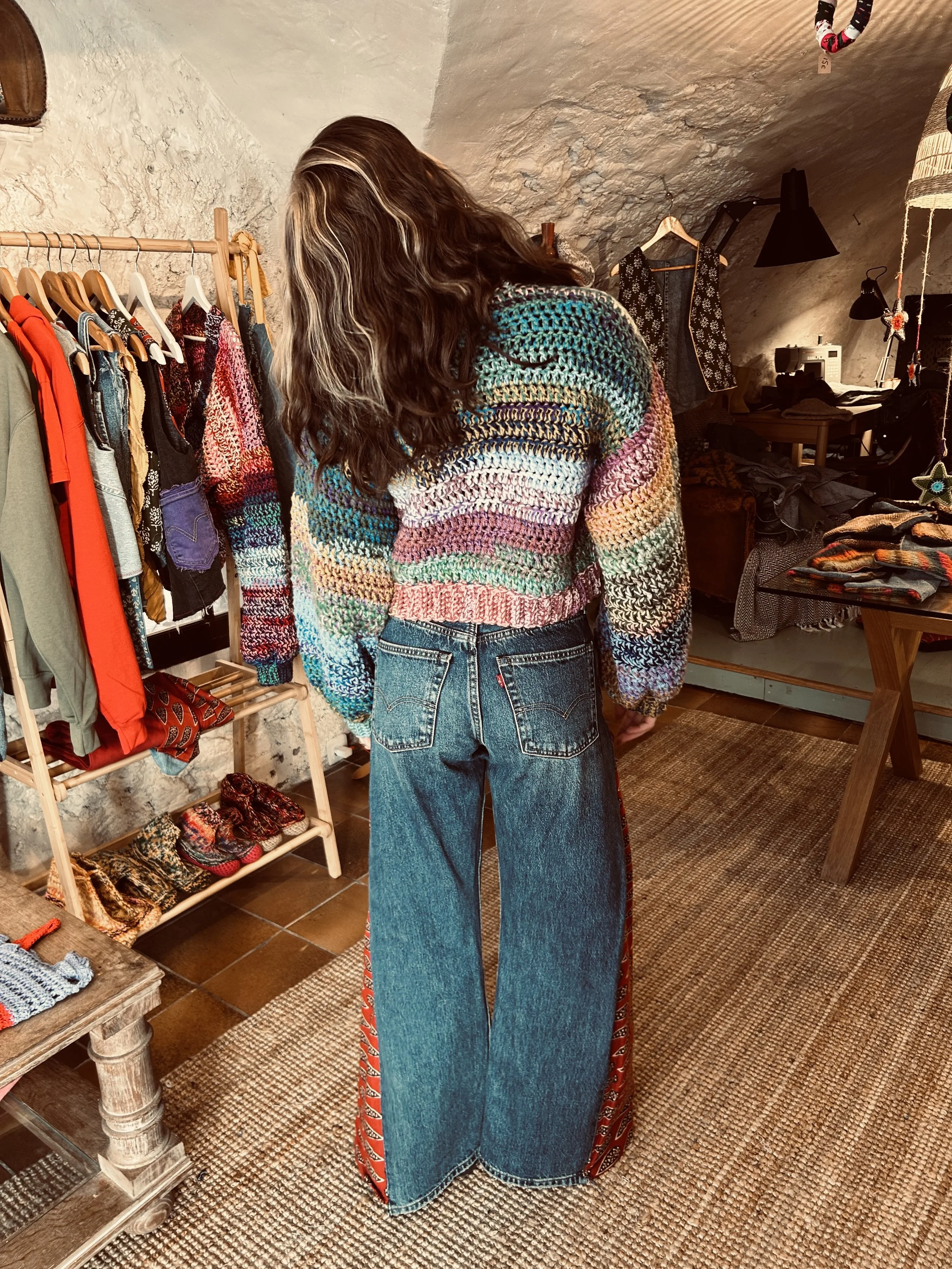 Femme portant un pull en laine multicolore et un jean à taille haute dans une boutique de vêtements.