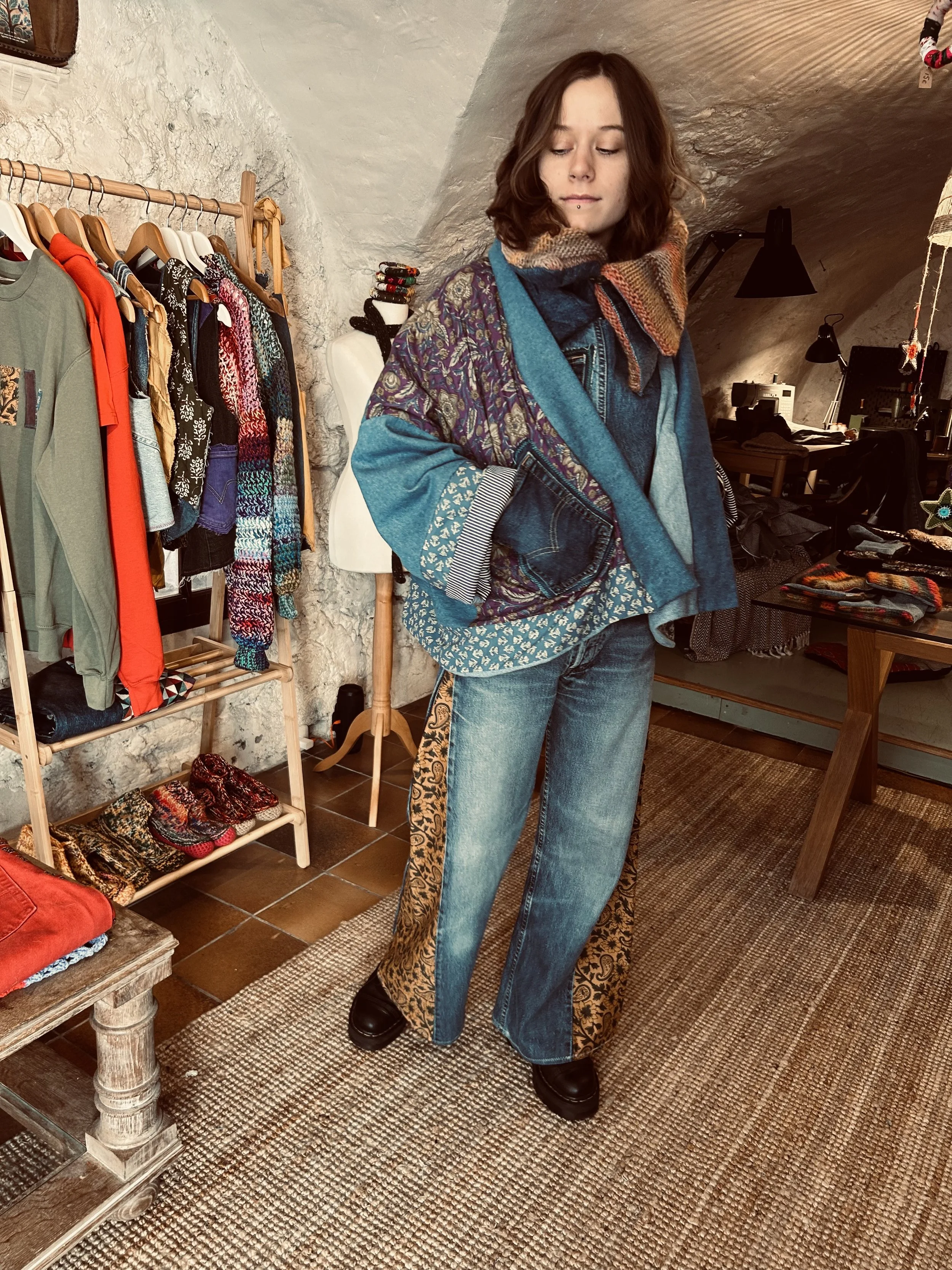 Une femme portant un manteau coloré et un foulard dans une boutique de vêtements vintage.