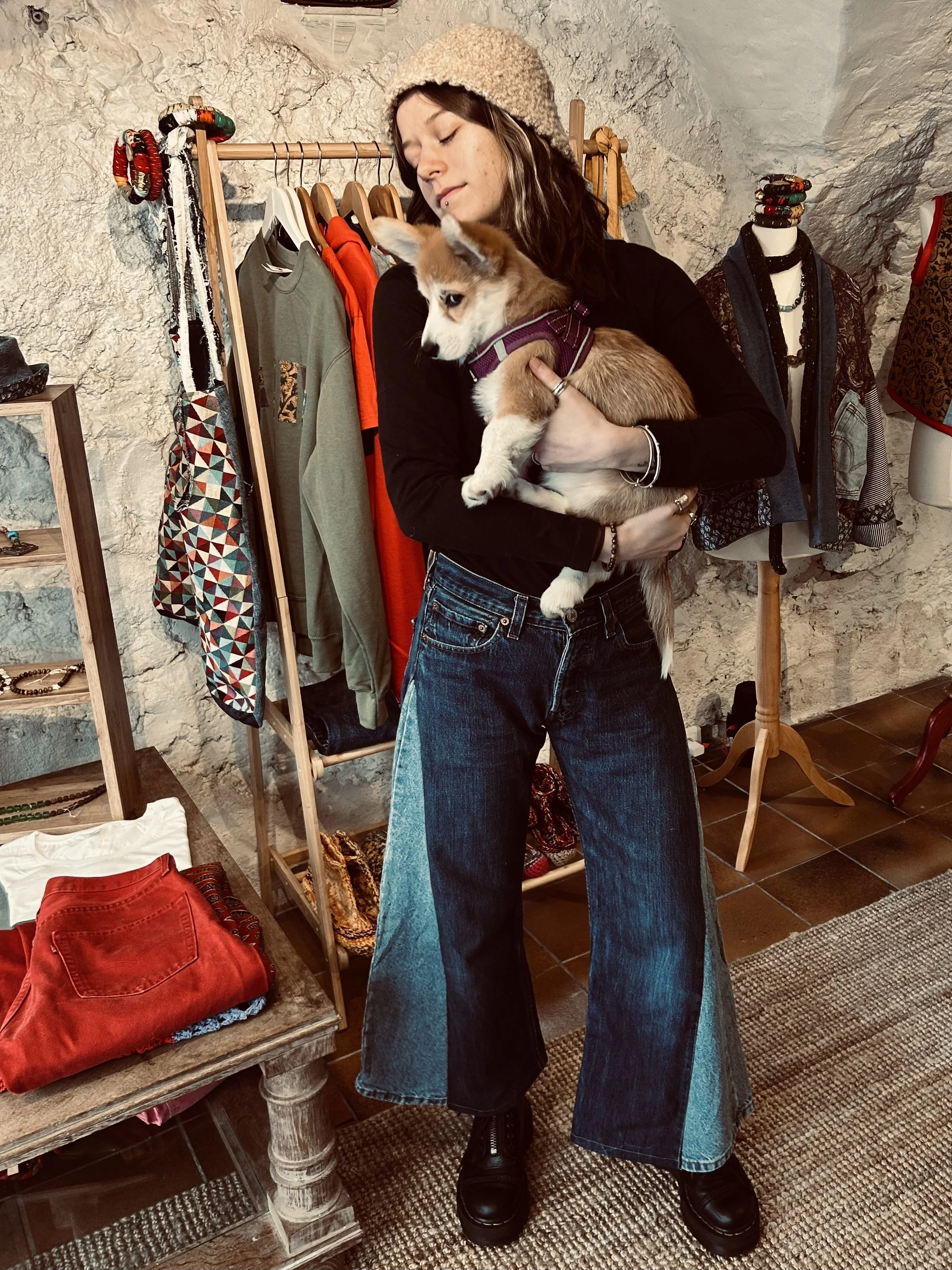 Une femme tenant un chiot dans un magasin de vêtements, avec des vêtements et des accessoires en arrière-plan.