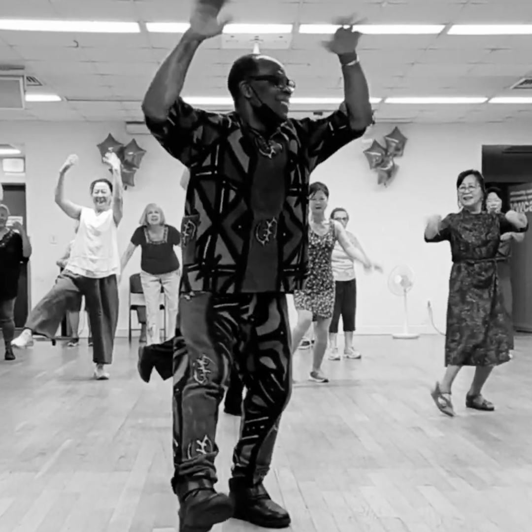 A group of people dancing and celebrating indoors, with a man in the foreground smiling and raising his arms.