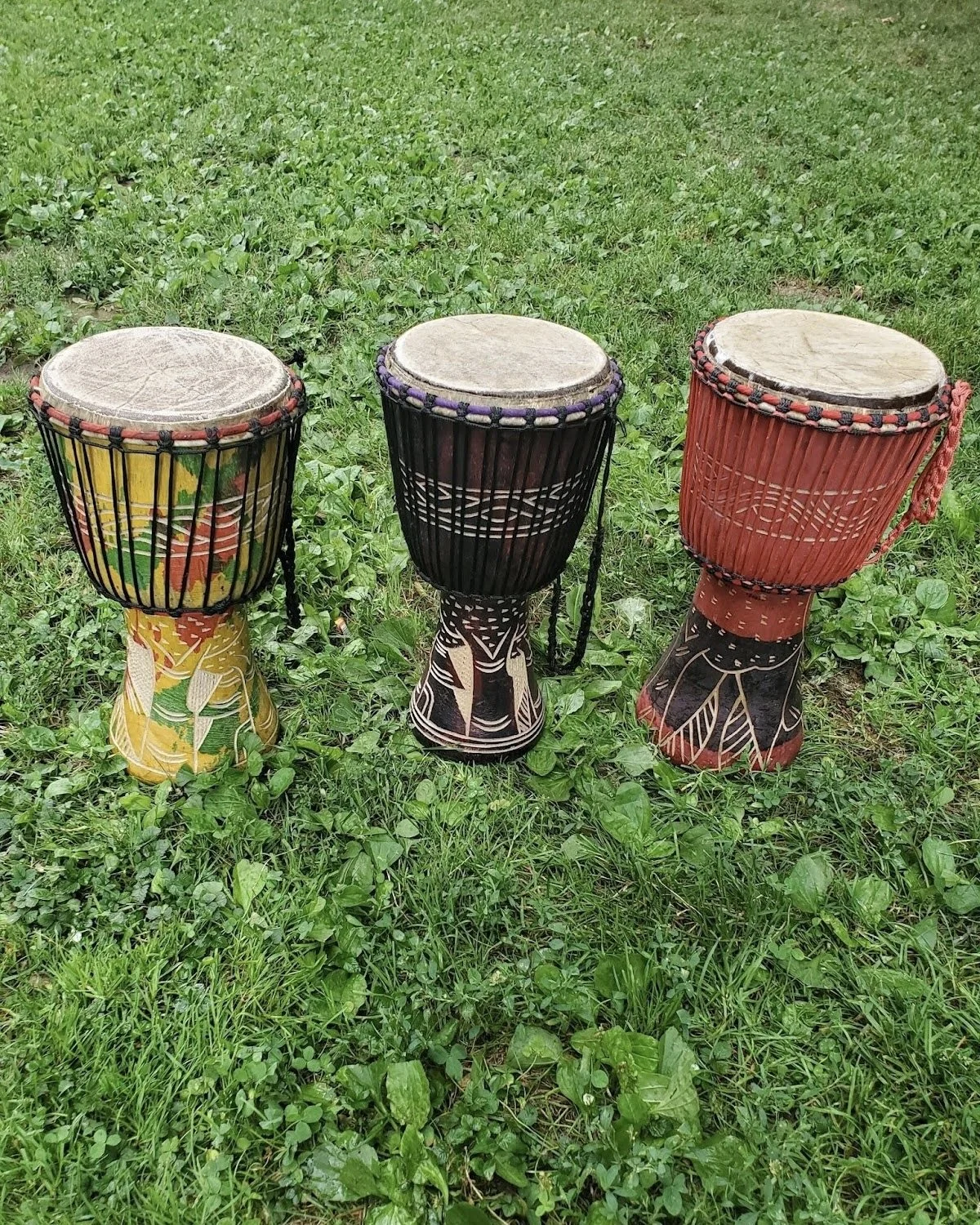 Three African hand drums with decorated bases and colorful Drum shells placed on grass.