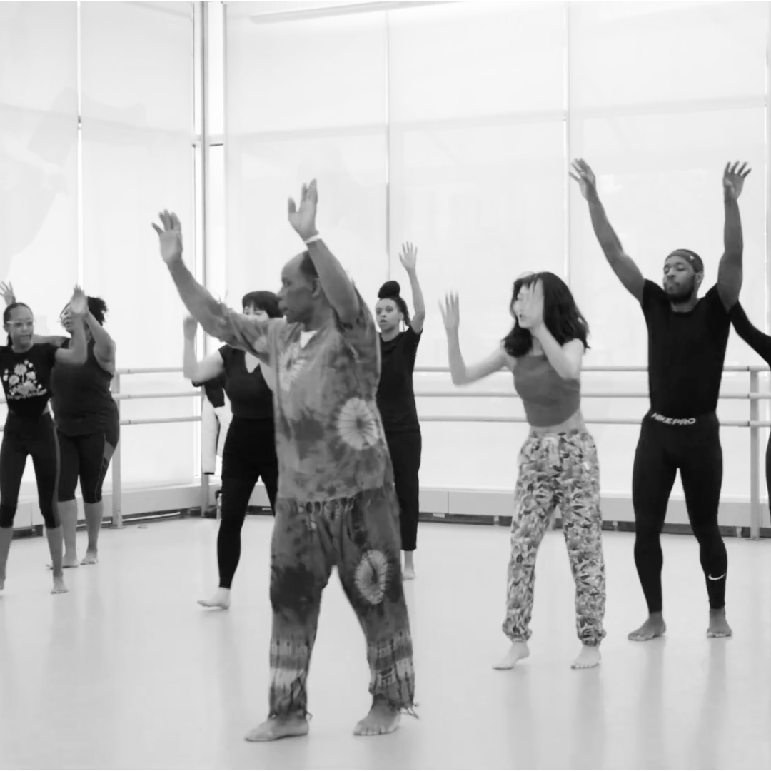 Group of people participating in a dance or movement class in a studio with large windows.