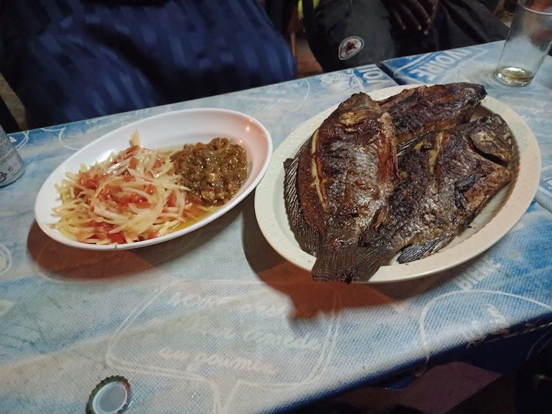 Plate of grilled fish with side of pickled vegetables and sauce on a table at a restaurant.