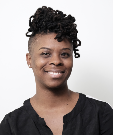 Portrait of a smiling woman with short natural hair styled in twists on top, wearing a black shirt with a white shoulder detail, against a plain white background.