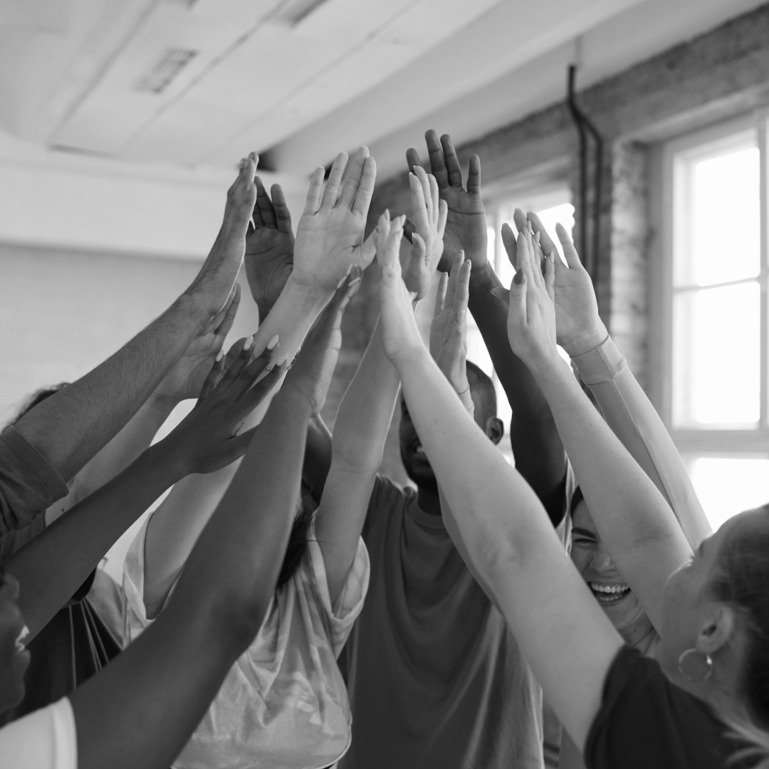 Group of diverse people in a circle giving high-fives and smiling indoors.