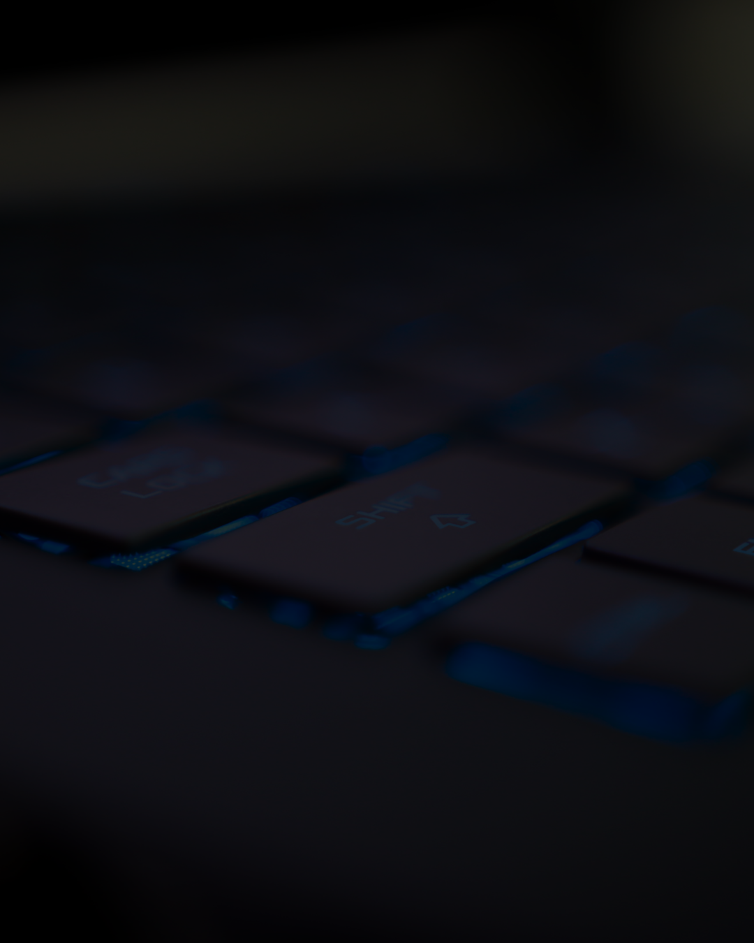 Close-up of a dark keyboard with backlit keys, partially illuminated.