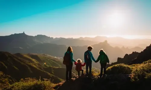 Family holding hands atop a mountain viewpoint at sunset, representing meaningful and memorable family travel adventures.