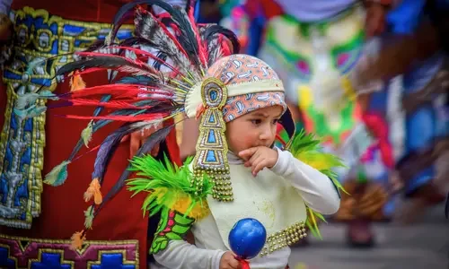 Young child dressed in vibrant traditional regalia at a cultural festival.