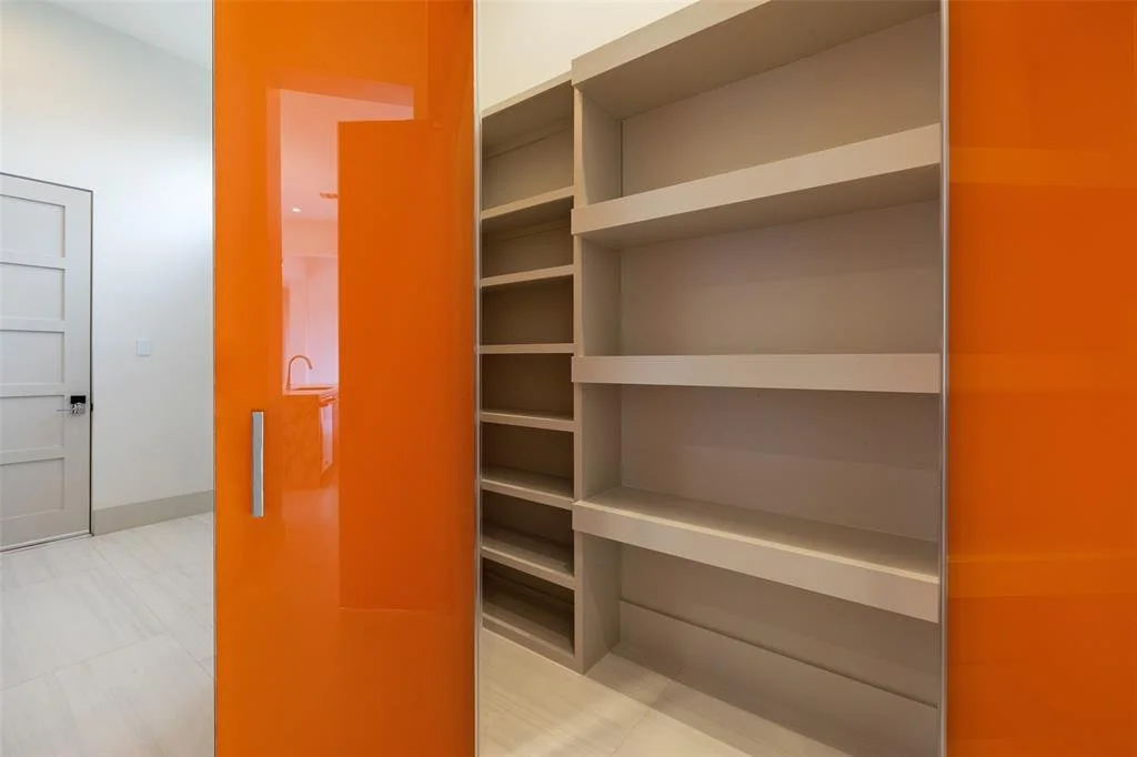 Interior view of a room with an orange sliding door on the left, beige shelves on the right, and a white door with paneled design in the background.