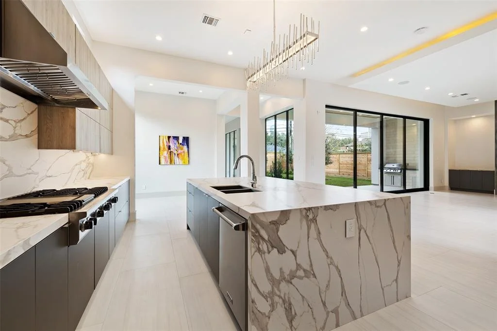 Modern open-concept kitchen with marble island, stainless steel appliances, and large sliding glass doors leading to a backyard.