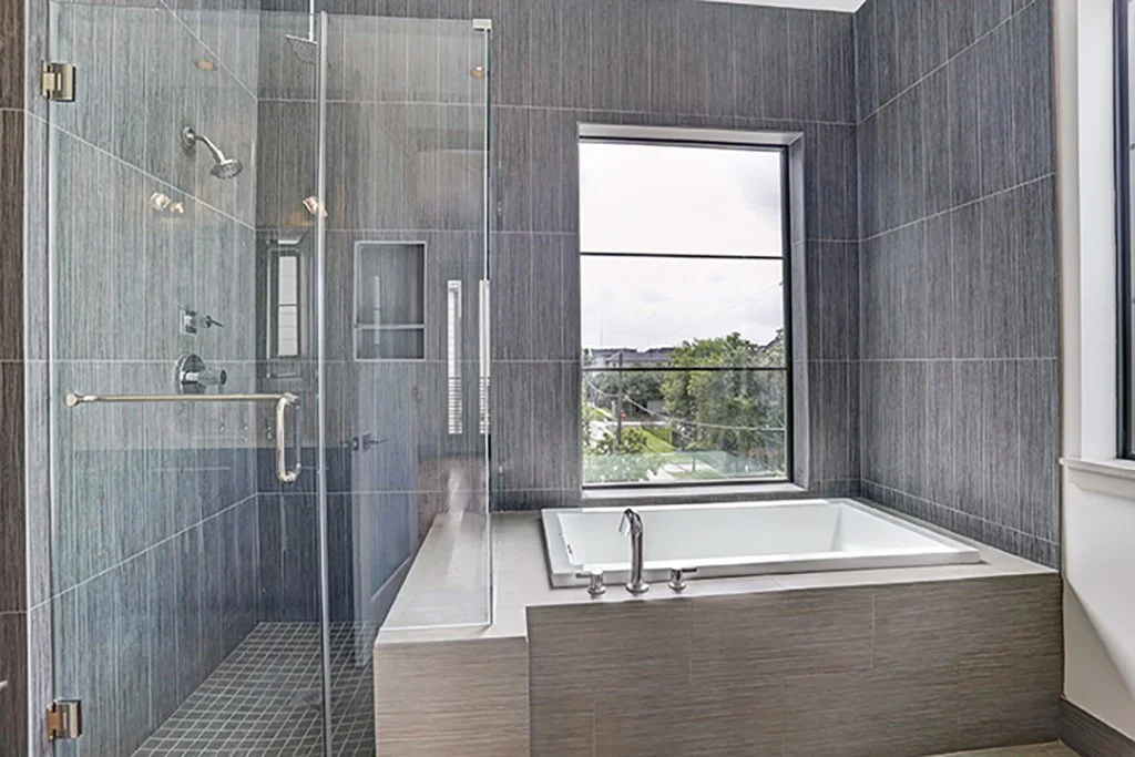 Modern bathroom with a walk-in glass shower and a built-in bathtub under a large window overlooking greenery.