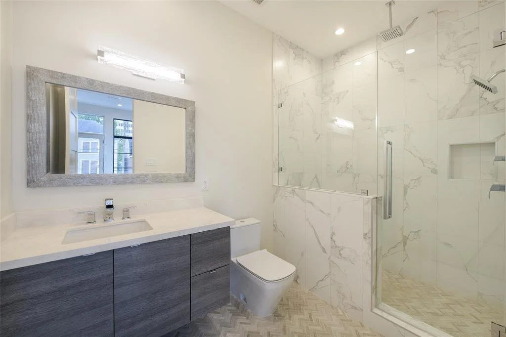Modern bathroom with vanity mirror, sink, toilet, and walk-in shower with marble tiles.