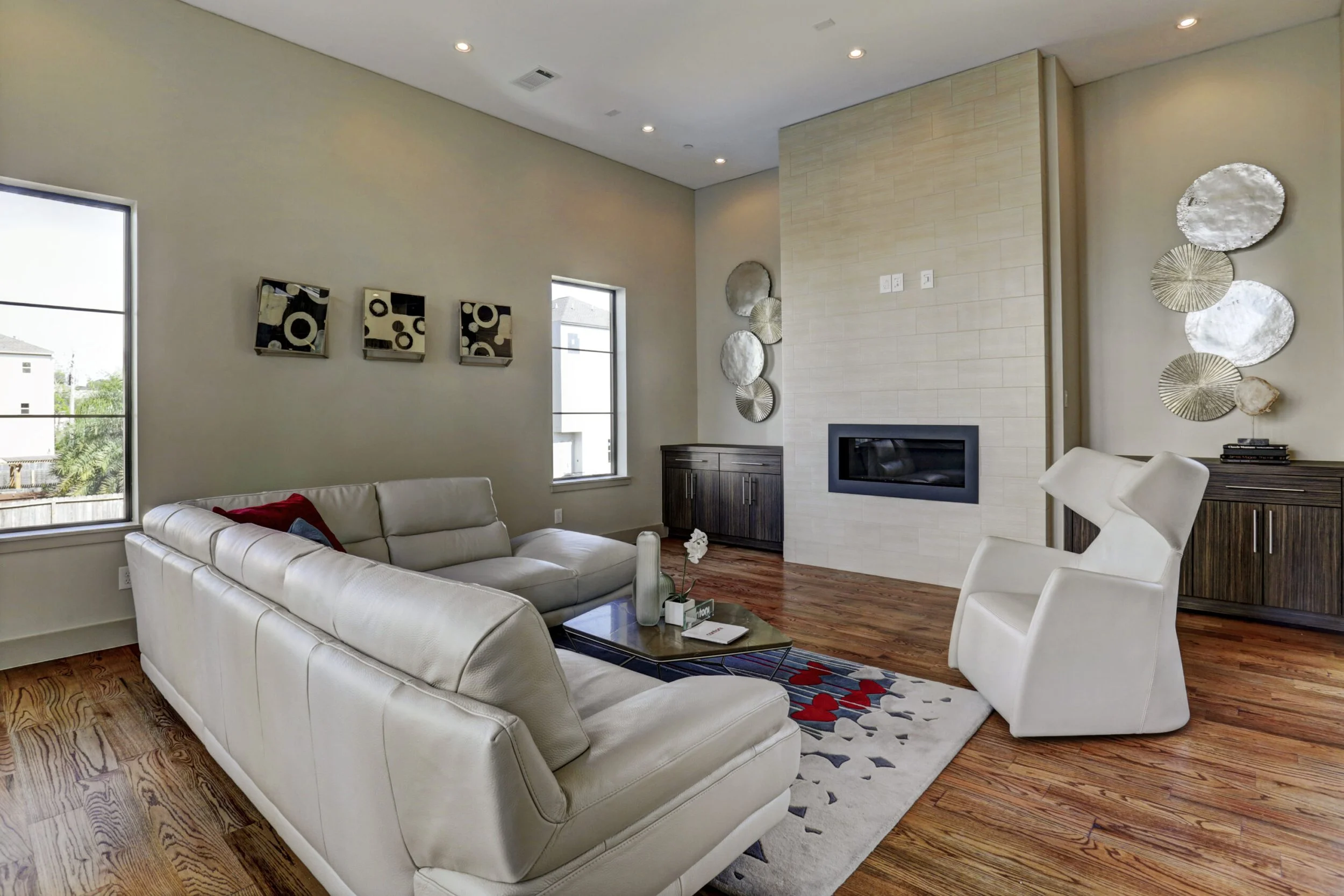 Modern living room with a white leather sectional sofa, white armchair, wooden flooring, and decorative wall art.