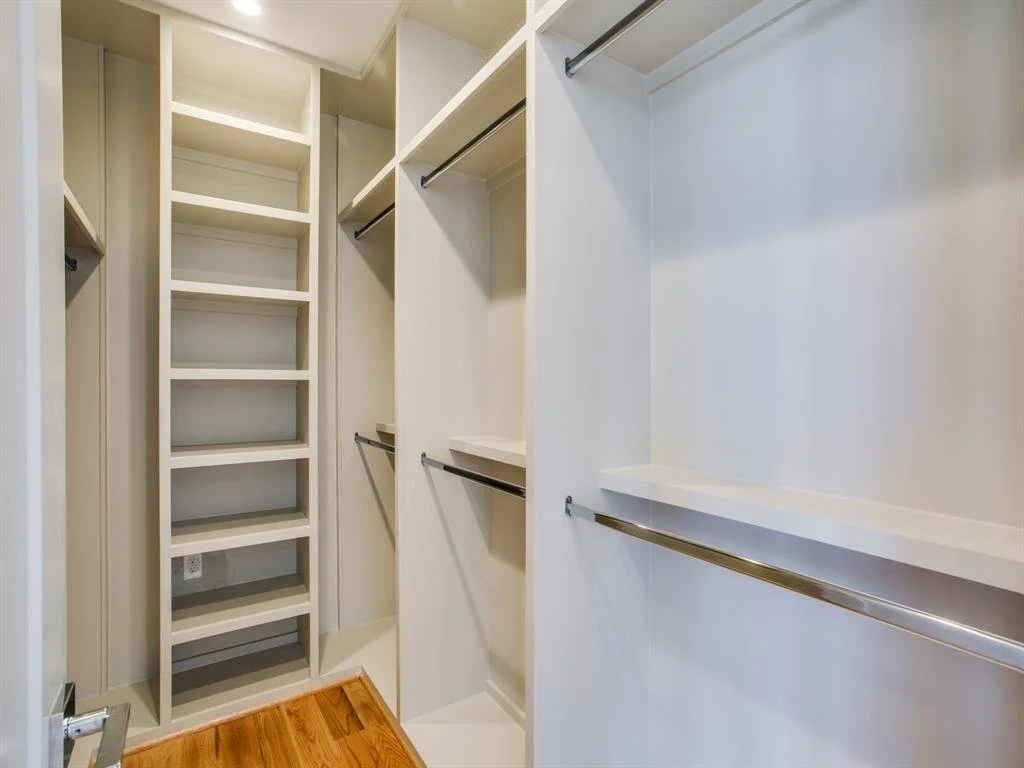 Empty walk-in closet with built-in shelves and hanging rods, hardwood floor, and neutral-colored walls.