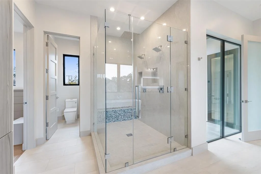 Modern bathroom with a glass-enclosed shower, a separate toilet area, and sliding glass doors.