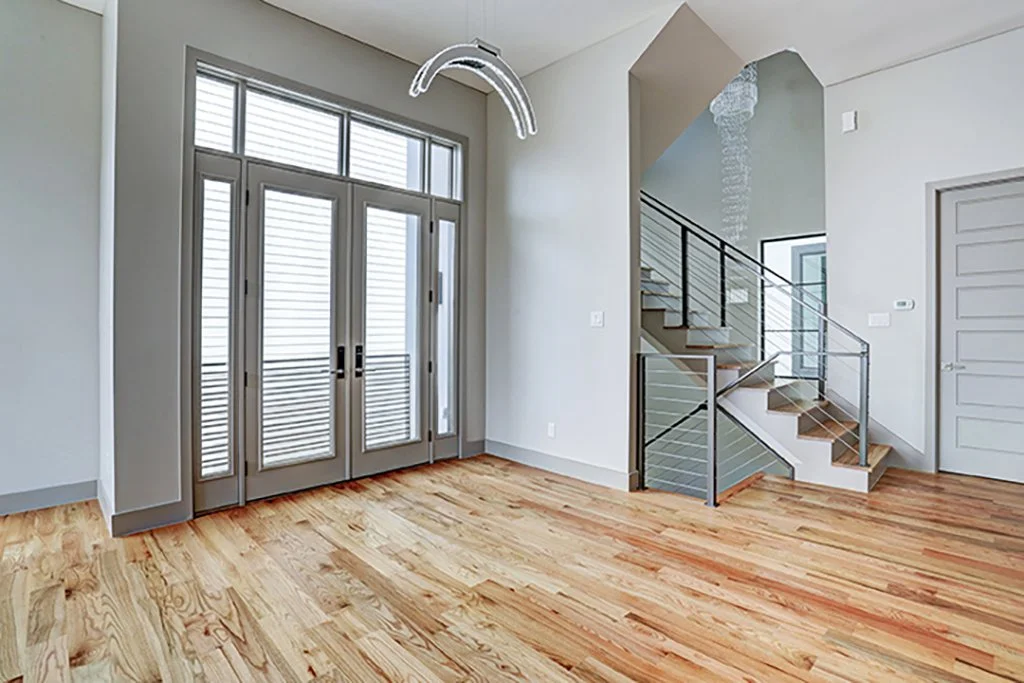 Empty living room with hardwood floors, large front door with sidelights and a staircase with metal railing.
