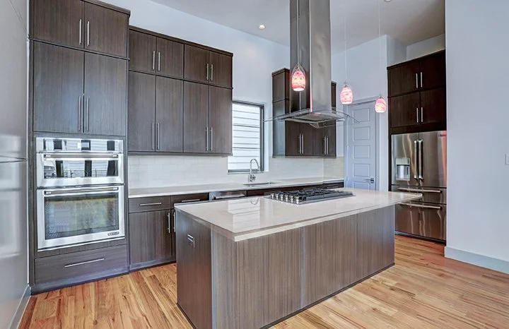 Modern kitchen with dark wood cabinets, stainless steel appliances, a center island with a white countertop, and pendant lighting.