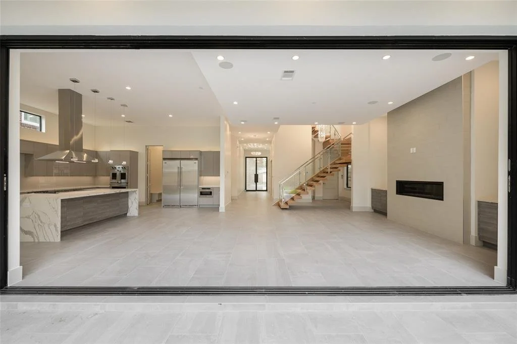 Empty modern kitchen and living room with a staircase, stainless steel appliances, and large sliding glass doors.