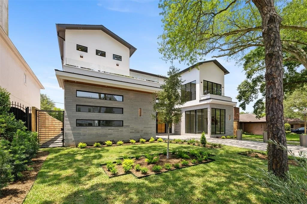 Modern two-story house with large glass windows, surrounded by a well-maintained lawn and trees.