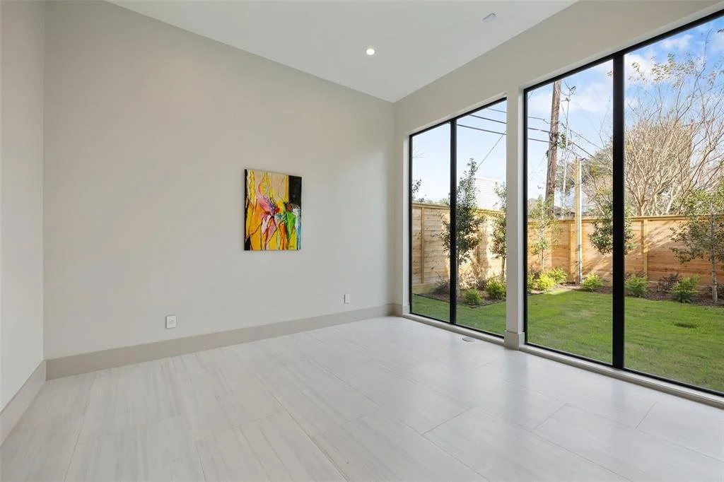 Empty room with large glass sliding doors overlooking a backyard with trees and a wood fence.