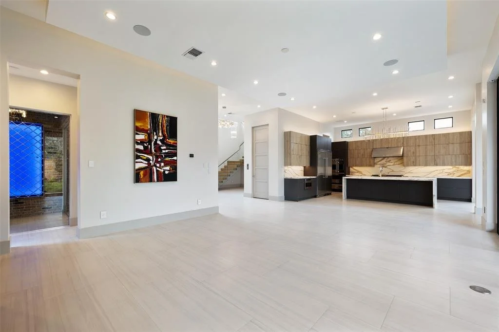 Open-concept modern kitchen and living space with white walls, light flooring, wooden cabinets, black appliances, and abstract wall art.