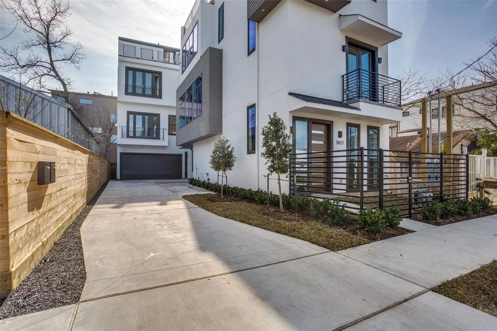 Modern multi-story residential building with a driveway, small landscaped yard, and balcony.