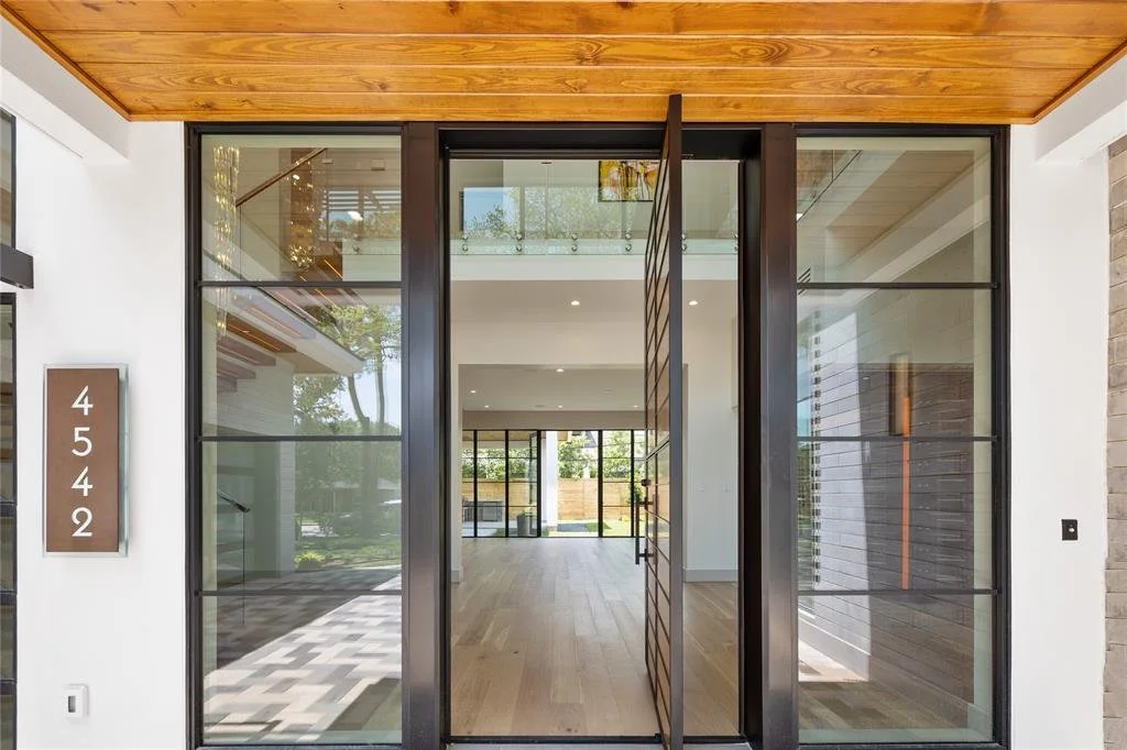 Modern entrance with large glass doors and windows, light wooden flooring, and a house number sign '4542' on a wall.