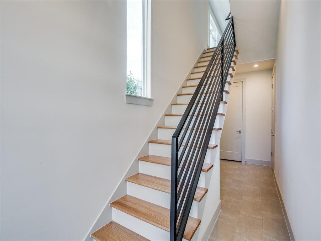 Indoor staircase with wooden steps and black metal railing, next to a window, in a modern home interior.