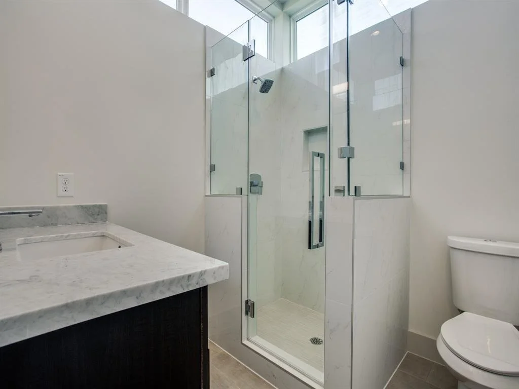 Modern bathroom with glass shower enclosure, white marble countertop, and toilet.