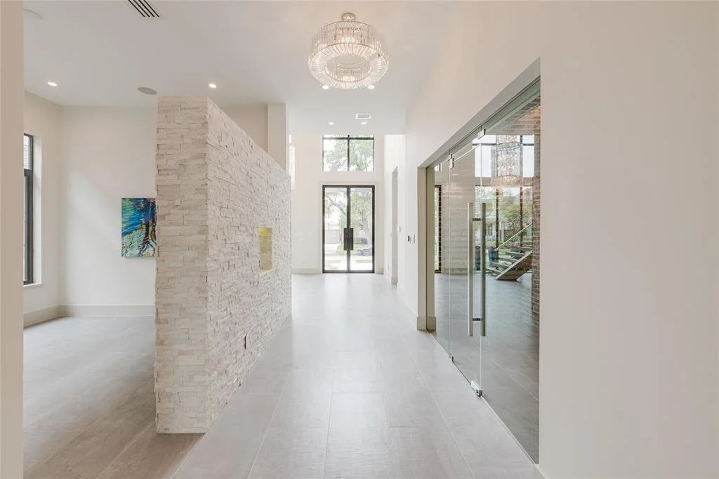 Modern interior with white walls, large windows, a crystal chandelier, a white brick partial wall, and a glass door leading to an outdoor area with stairs.