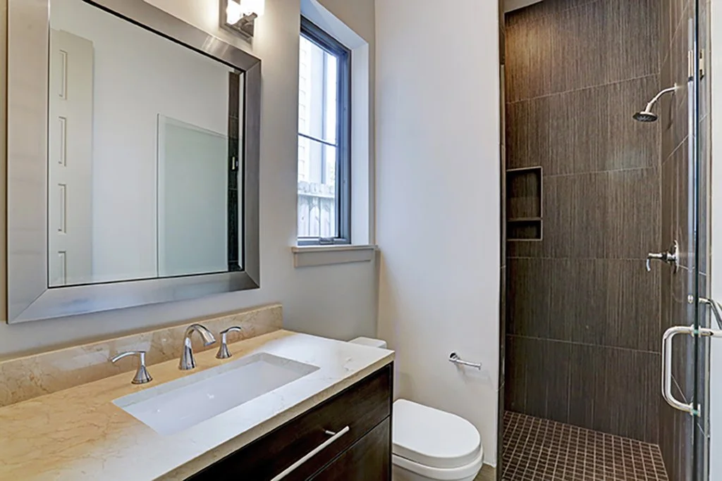 Modern bathroom with a vanity sink, large mirror, small window, and a walk-in shower with brown tiles.