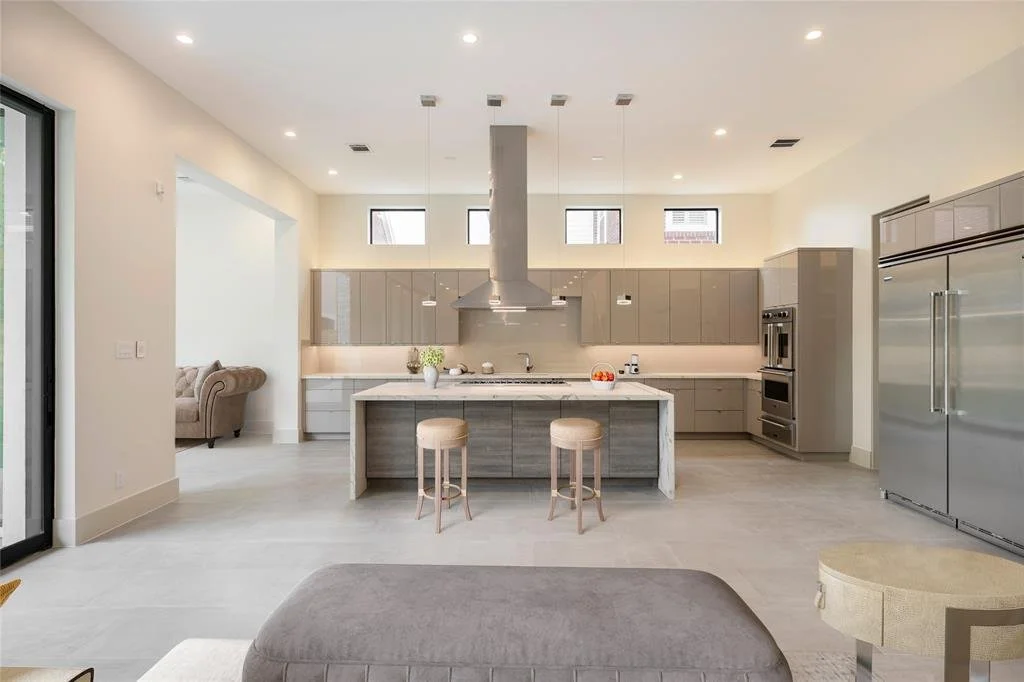 Modern kitchen with gray cabinets, stainless steel appliances, a large island with two stools, and a spacious open layout.