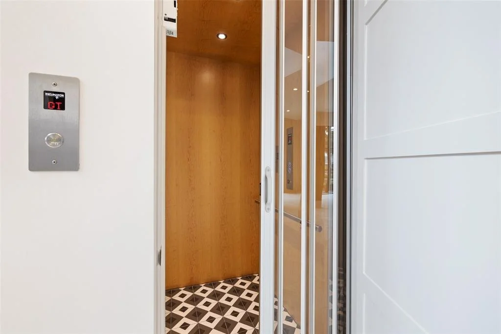 Interior of an elevator with wooden walls, glass door, and patterned black and white floor tiles.