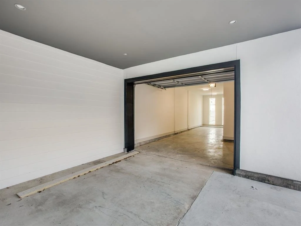 An empty garage with an open door leading into a bright interior room with a window and door.